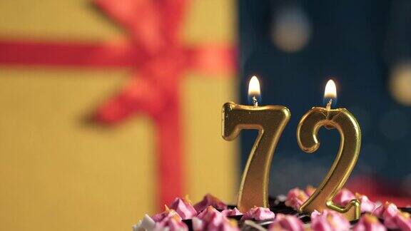 72号生日蛋糕用金色蜡烛点燃蓝色背景的礼物用黄色礼盒系上红丝带特写和慢动作