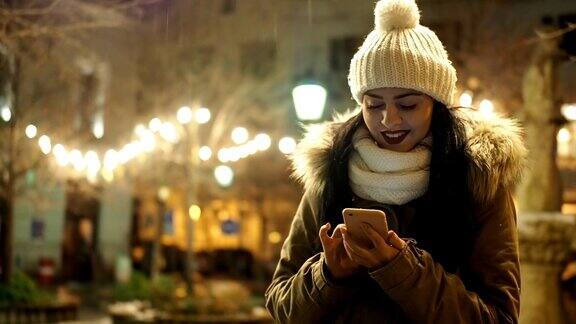 美丽的女孩拿着手机在冬天的街道上与圣诞灯-慢镜头