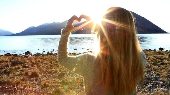 湖边的一名年轻女子在山湖景观上做了一个心形的指架