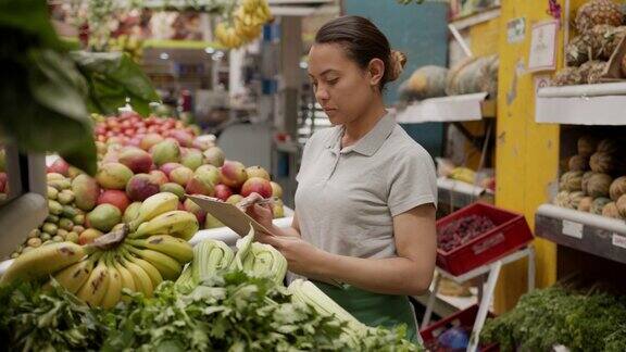 拉丁美洲的女售货员正在她的市场摊位上用写字板清点蔬菜