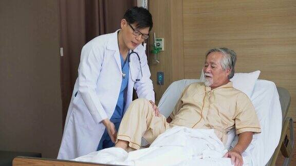 一位年轻的亚洲医生在医院医务室的病床上检查这位老人手术后的膝盖和腿