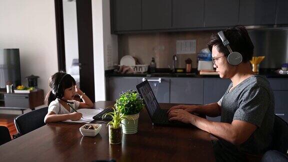 年轻的亚洲可爱的女孩在家里用笔记本电脑学习在流行病期间与她的父亲在客厅