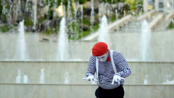 滑稽的哑剧在红色贝雷帽弹钢琴在喷泉背景