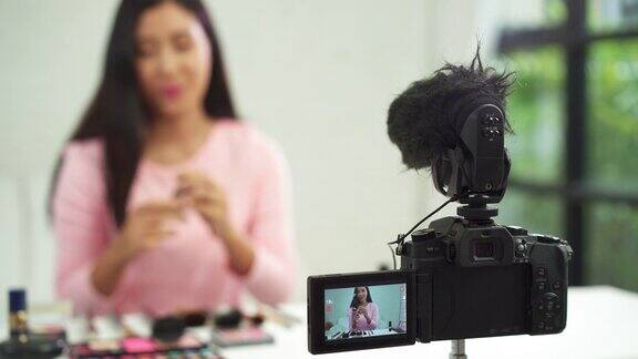 美妆博主坐在镜头前录制视频展示美妆美女一边用刷子复习化妆教程一边通过互联网到社交网络直播视频
