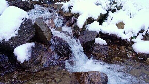 在乌克兰风景如画的喀尔巴阡山脉中一条小溪在潮湿的石头和白雪中流淌