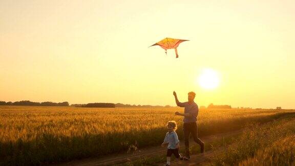 日落时分父亲和儿子在大自然中玩风筝家庭和户外娱乐的统一幸福的家庭慢动作