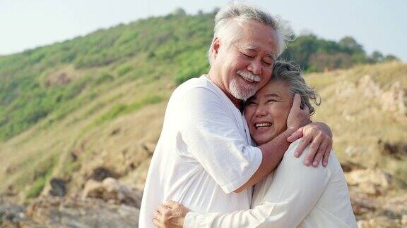 4K亚洲老年夫妇拥抱在悬崖上在夏天的日落