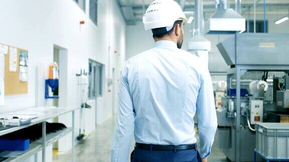 背影镜头的总工程师在安全帽走过轻型现代工厂同时拿着笔记本电脑现代工业环境下的成功英俊男人