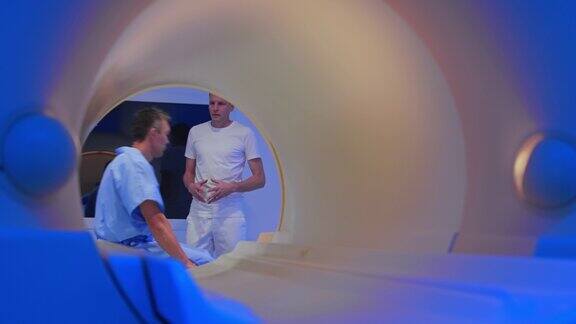 男性病人坐在核磁共振成像仪的桌子上和医生交谈
