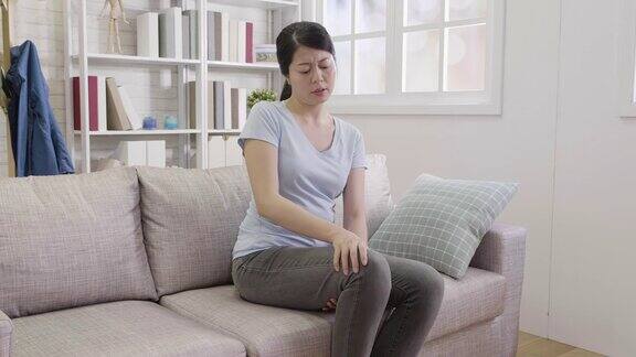 一个女人坐在沙发上忍受着腿部疼痛