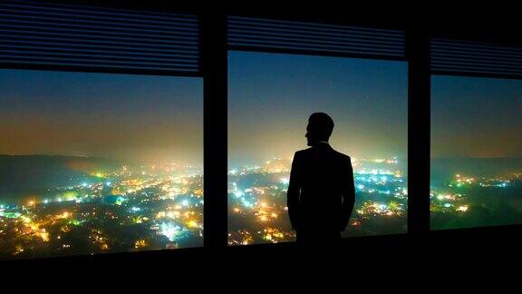 这名男子站在一扇窗旁背景是夜色中的城市时间流逝