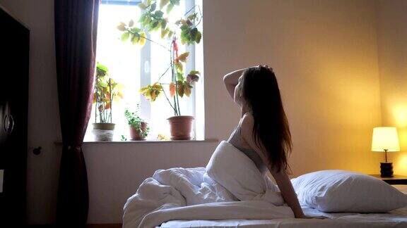 一个女人早上醒来坐在床上伸懒腰摸着自己的头发
