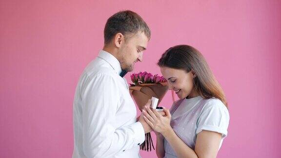 穿着优雅的男子正在给微笑着的幸福年轻女子送花和戒指