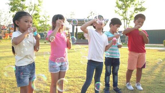在阳光明媚的夏日里一群快乐的亚洲小朋友在公园的草地上一起吹泡泡