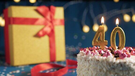 白色生日蛋糕40支金色蜡烛用打火机点燃蓝色背景用彩灯黄色礼盒用红丝带系好特写镜头