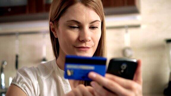 穿着白色t恤的美女用手机信用卡在网上购物厨房