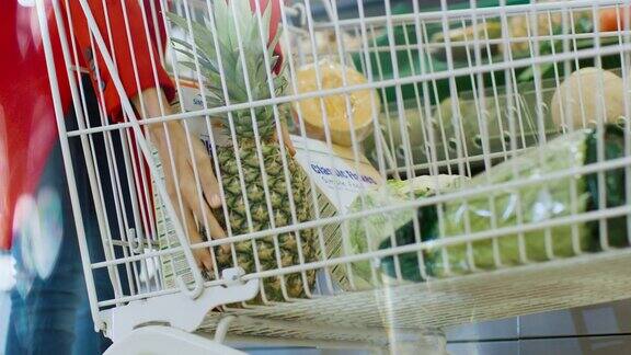 在超市:低角度拍摄的女人从新鲜农产品区拿有机菠萝并把它放进购物车
