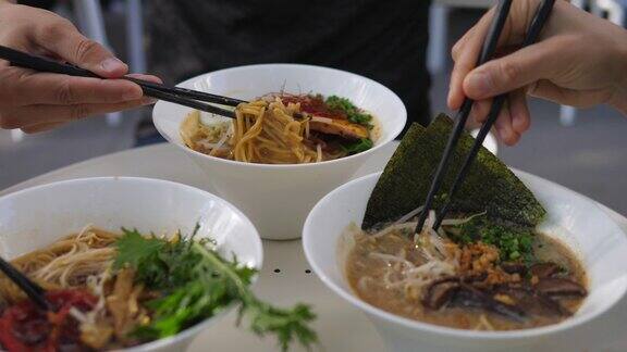 素食的亚洲美食三个人用筷子在拉面汤中搅拌配料的侧面图