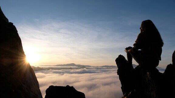 一个女旅人坐在山顶上看日出和雾海
