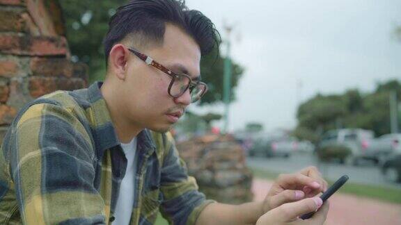 慢镜头一名亚洲男子在泰国大城府度假旅行后一边放松一边用智能手机查看社交媒体马累在传统城市的惊人地标处享受他的旅程