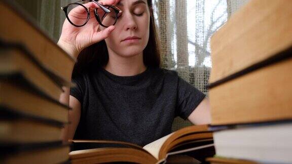 疲惫的年轻女子摘掉眼镜在阅读纸质书后按摩眼睛女学生因长时间戴眼镜而感到不适患眼睛疼痛或头痛