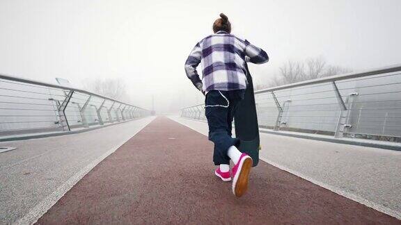 后视图一个男性滑板运动员跑起来站在长板上一个雾蒙蒙的早晨一个年轻人在桥上骑滑板