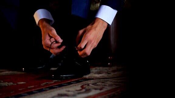 身着深蓝色夹克的男子将鞋带系在黑色漆皮皮鞋上