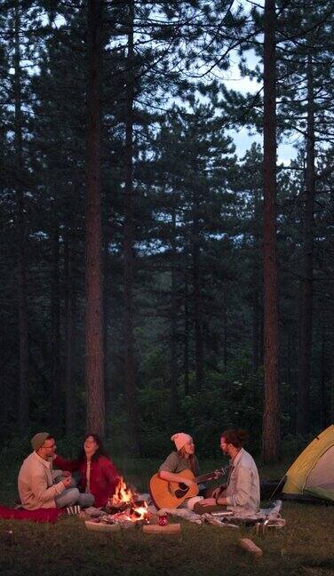 垂直视频一群快乐的朋友一起露营在树林里唱歌和弹吉他