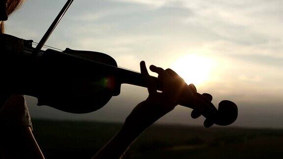 剪影少女小提琴家拉小提琴在日落天空的背景