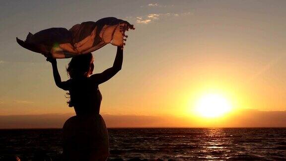 日落时分在海滩上围着围巾的女人的剪影