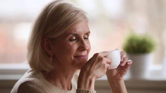 平静快乐的老妇人独自坐着拿着杯子享受着咖啡