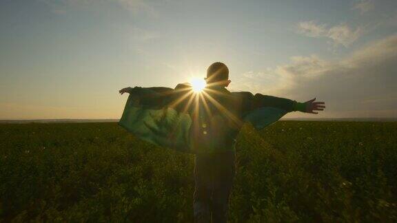一个穿着绿色斗篷的男孩超级英雄正在田野上奔跑日落4k