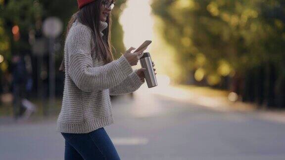 拿着杯子和智能手机走在街上的女孩