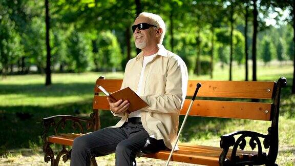 快乐的盲人老人阅读有趣的故事在盲文书享受休息在公园