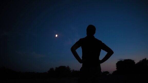 一个男人的剪影和乡村星空下年轻的月亮