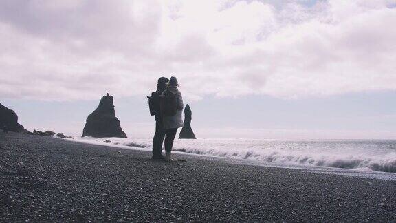 一对年轻的夫妇在冰岛的黑沙滩上手拉手慢镜头