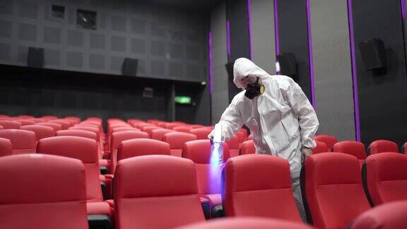 亚洲华人电影卫生员在电影放映前在影院的椅子和地毯上戴口罩进行消毒
