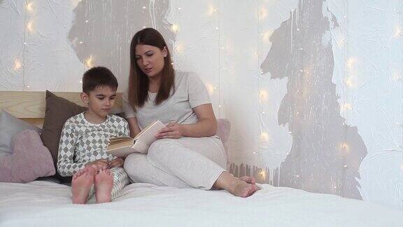 穿着睡衣的漂亮女孩坐在床上给一个小男孩读书然后上床睡觉