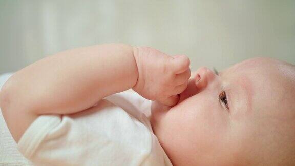婴儿躺在家里的床上吃手指和打哈欠