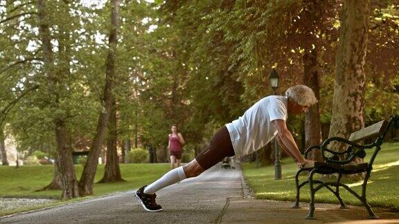 一位老人在公园长凳上做俯卧撑
