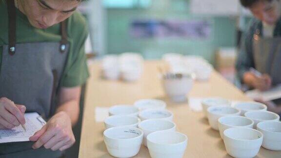 专业的亚洲华人咖啡师鉴赏家评分员表演咖啡杯和他的同事品尝咖啡杯后写在剪贴板上