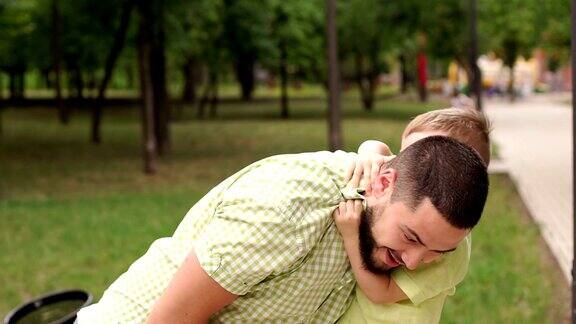 年轻的爸爸抱着他可爱的小儿子在公园里背景是绿树