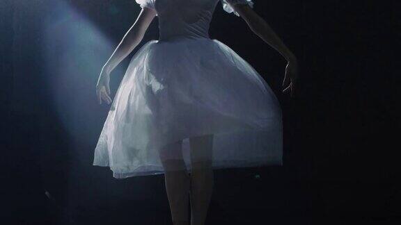 特写镜头的芭蕾舞女演员的腿在黑暗中她穿着芭蕾舞鞋在聚光灯下跳舞她穿着白色芭蕾舞裙在缓慢的运动