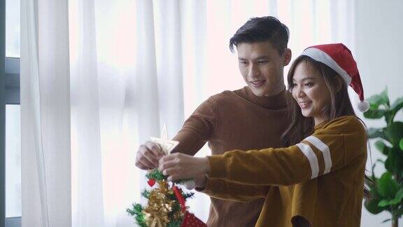 年轻的亚洲华人夫妇在装饰圣诞树时接吻庆祝圣诞节