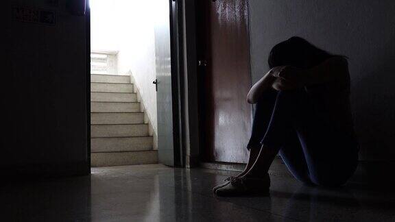 一个悲伤的年轻女孩的剪影坐在黑暗中靠在旧公寓的墙家庭暴力家庭问题压力暴力抑郁和自杀