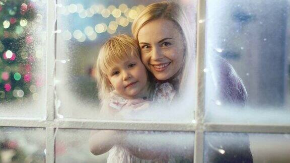 在平安夜妈妈和女儿透过白雪的窗户看花环在窗户上闪闪发光