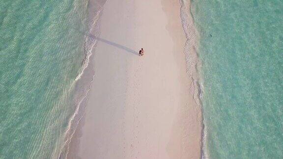 一对年轻的成年夫妇在马尔代夫的沙滩上一起走在碧绿的海水上