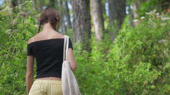 年轻女子在绿色的森林中漫步拿着白色的袋子