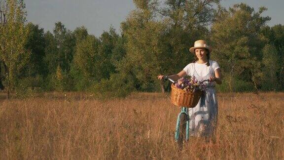 美丽的年轻女子与梦幻和浪漫的眼睛走和滚动复古自行车沿草地在阳光日落时分一个漂亮的女孩骑着一辆旧自行车带着花篮在田野里散步