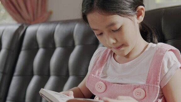 亚洲小女孩坐在沙发上看书呆在家里她翻开了学习的书女孩学习教育书籍